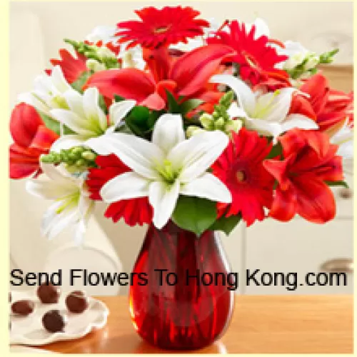 Gerbéras rouges, lys blancs, lys rouges et autres fleurs assorties disposées magnifiquement dans un vase en verre