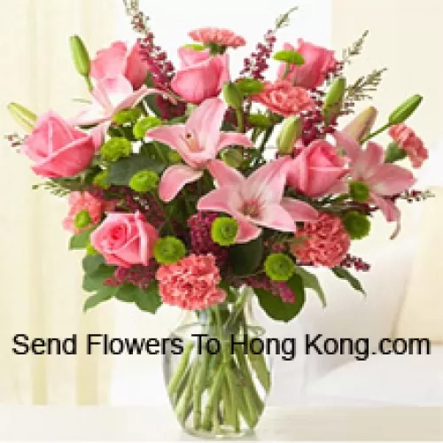 Roses roses, œillets roses et lys roses avec des fougères assorties et des garnitures dans un vase en verre